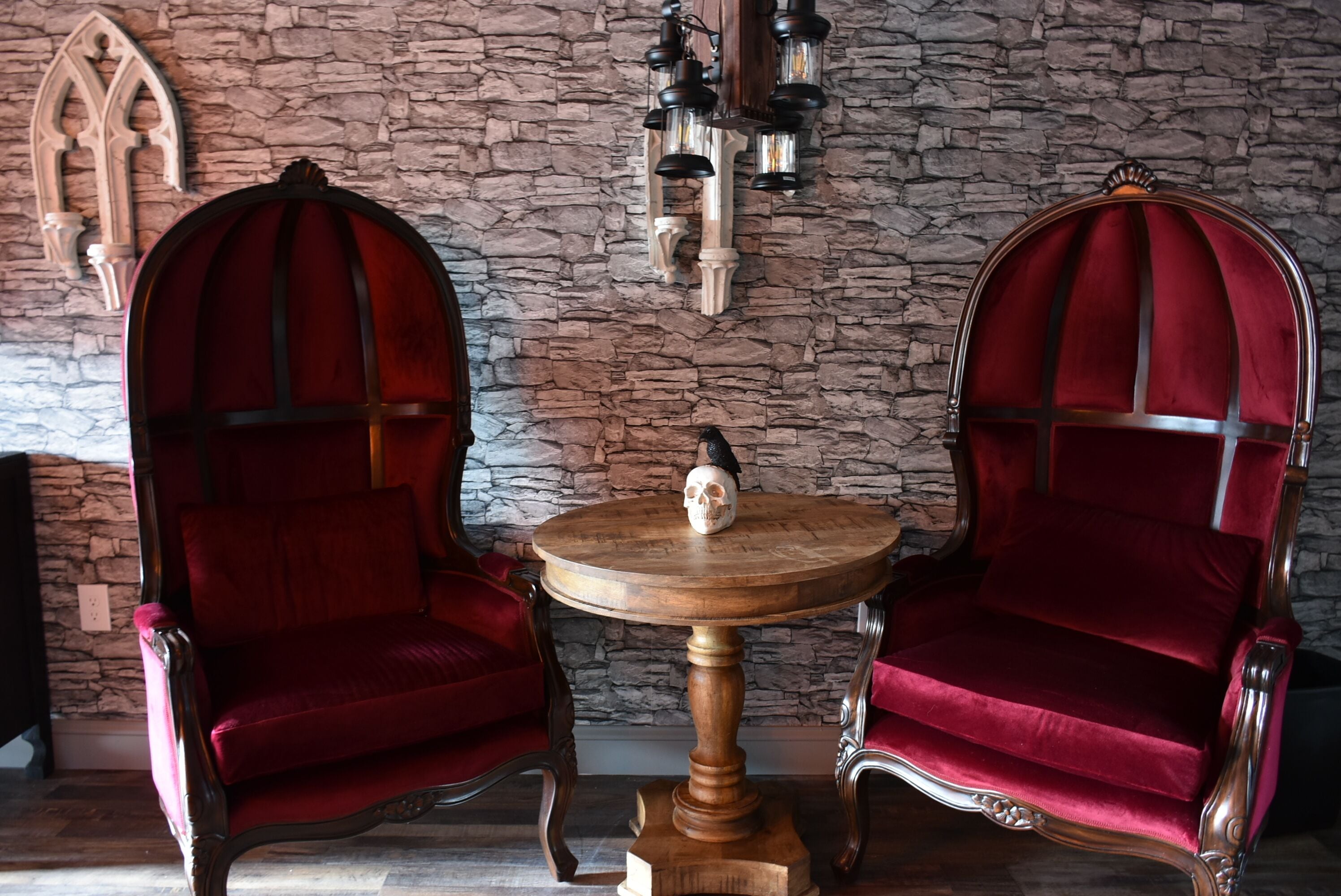 Two red velvet chairs with ornate wooden frames and a wooden table with a skull centerpiece.
