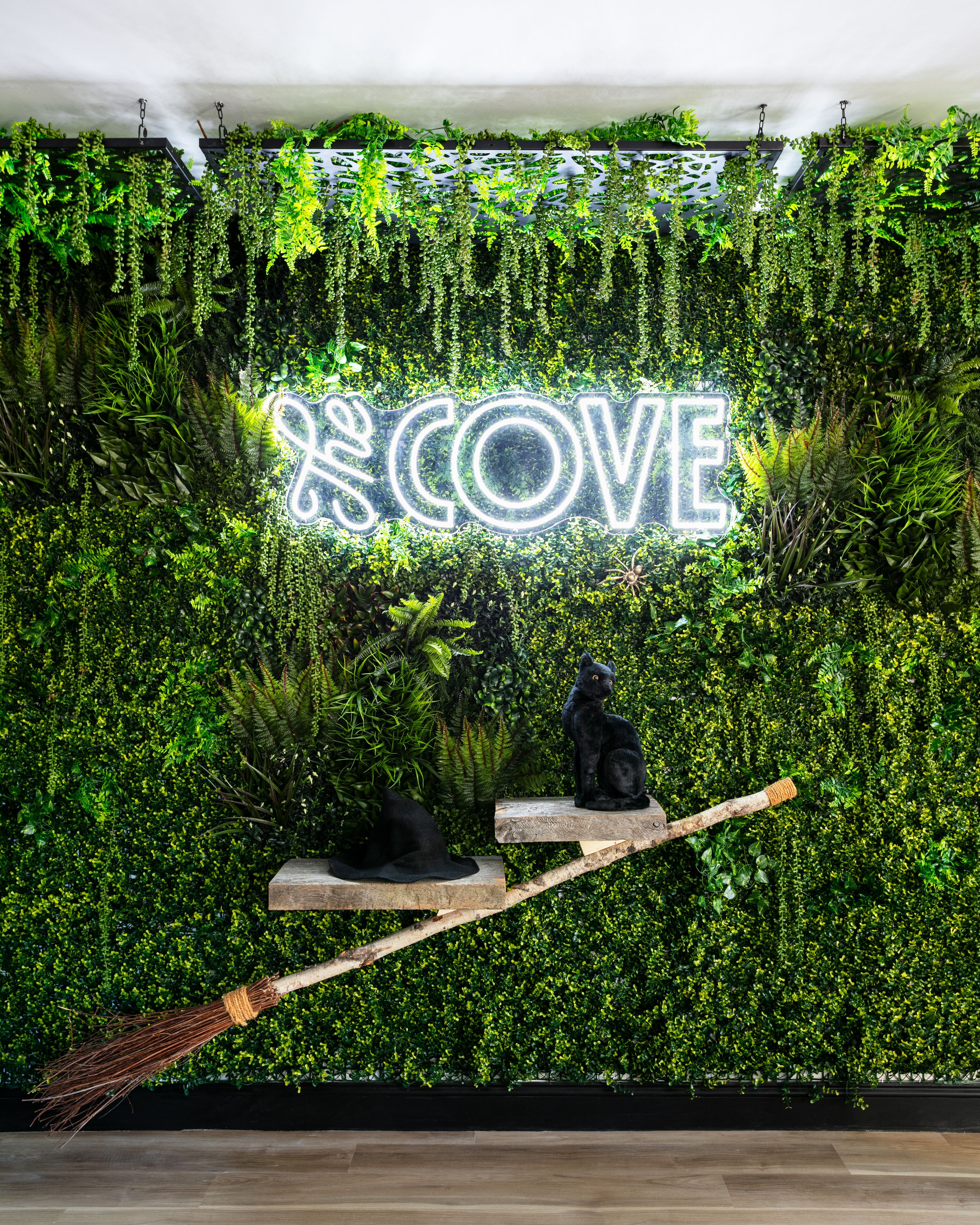 Pared con un letrero de neón que dice "COVE" rodeada de exuberante follaje verde.