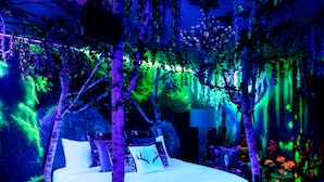 A bed in a room with a forest theme, including artificial trees and foliage. -  The Cove At Salem (Salem)