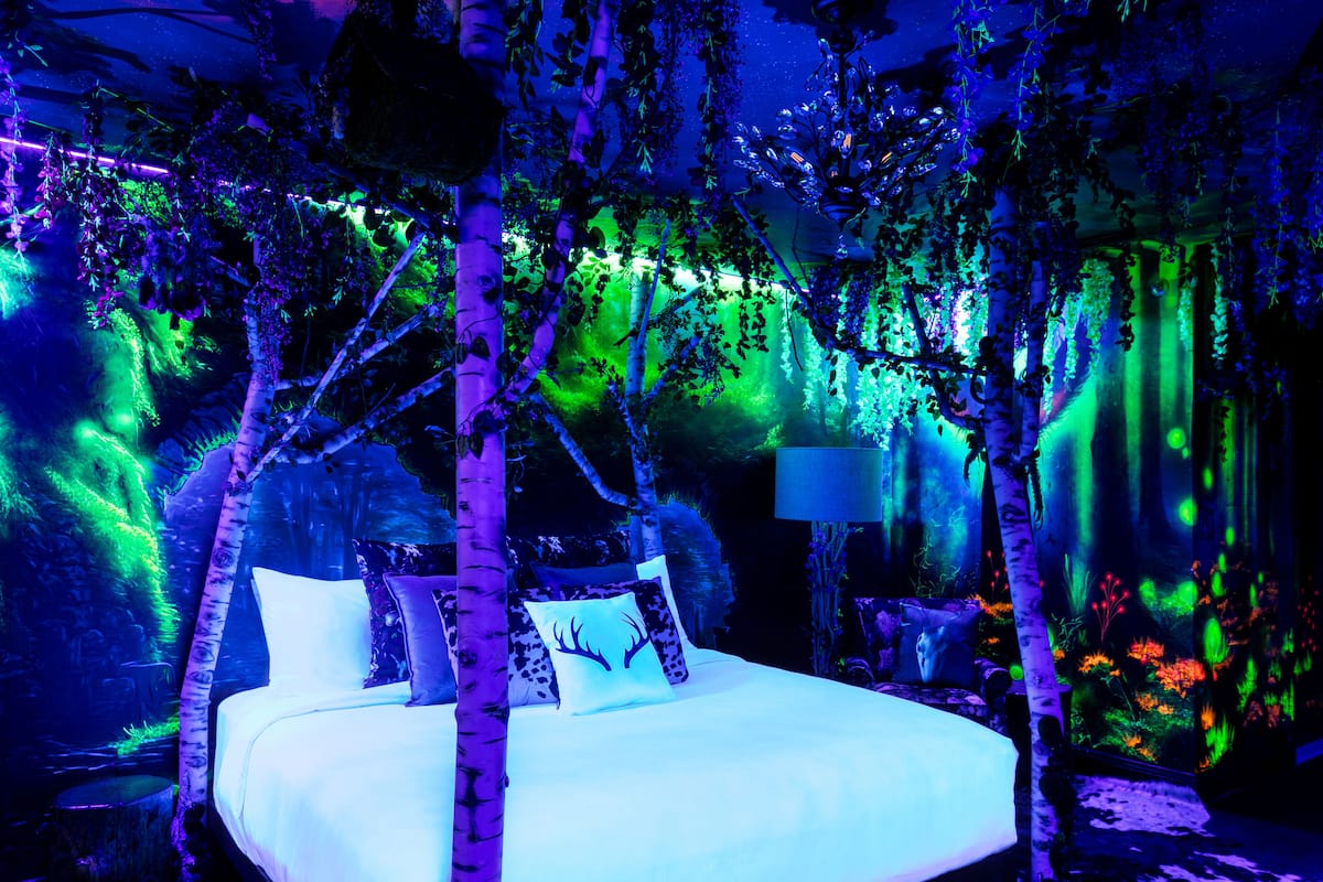 A bed in a room with a forest theme, including artificial trees and foliage.
