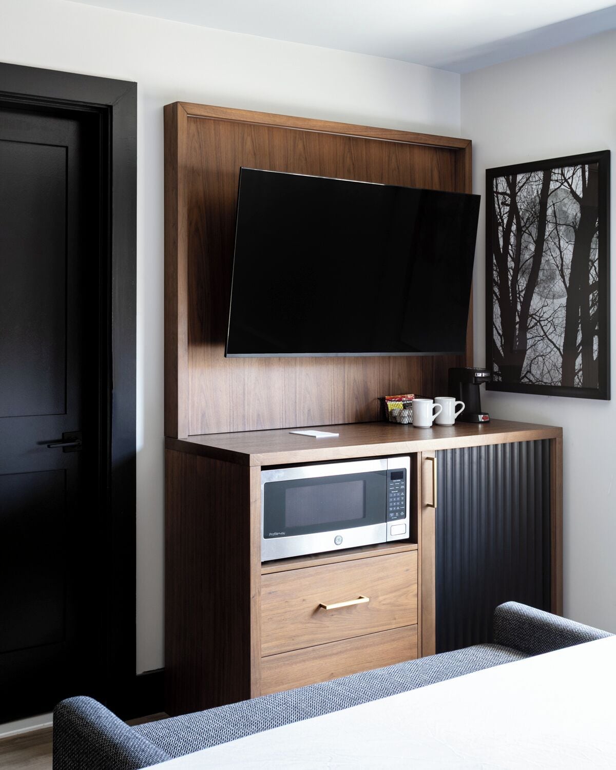 A compact kitchenette with a built-in microwave, a coffee maker, and a flat-screen TV mounted on a wooden cabinet.
