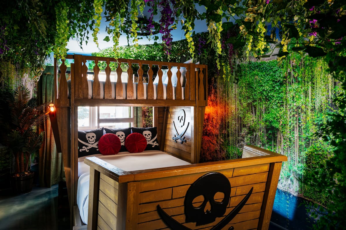 A bunk bed with a pirate-themed design, including skull and crossbones pillows, and a wooden headboard.