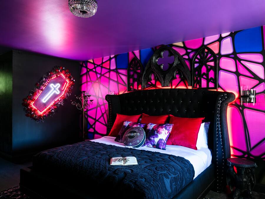 Un dormitorio con una cama, un letrero luminoso con una cruz de neón y un diseño geométrico en la pared.