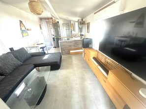 A modern living room with a sectional sofa, a flat-screen TV, and a kitchen area in the background.