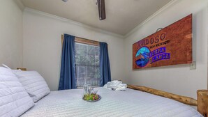 A neatly made bed with a white quilt, a bottle of water, and a plate of fruit on the nightstand. - Hunter's Lodge by Ruidoso Vacation Rentals (Ruidoso)