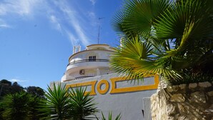 Un edificio blanco con detalles amarillos, un balcón y palmeras en primer plano.