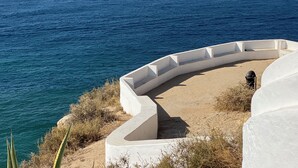 Estructura blanca y curvada con un banco a lo largo de un acantilado costero con vistas al mar.