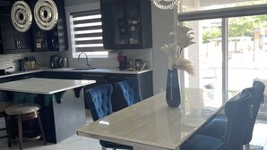 A modern kitchen with dark cabinetry, a central island, and a dining area with a glass table and blue upholstered chairs. - Luxury getaway with pool and hot tub - family retreat  (Windsor)