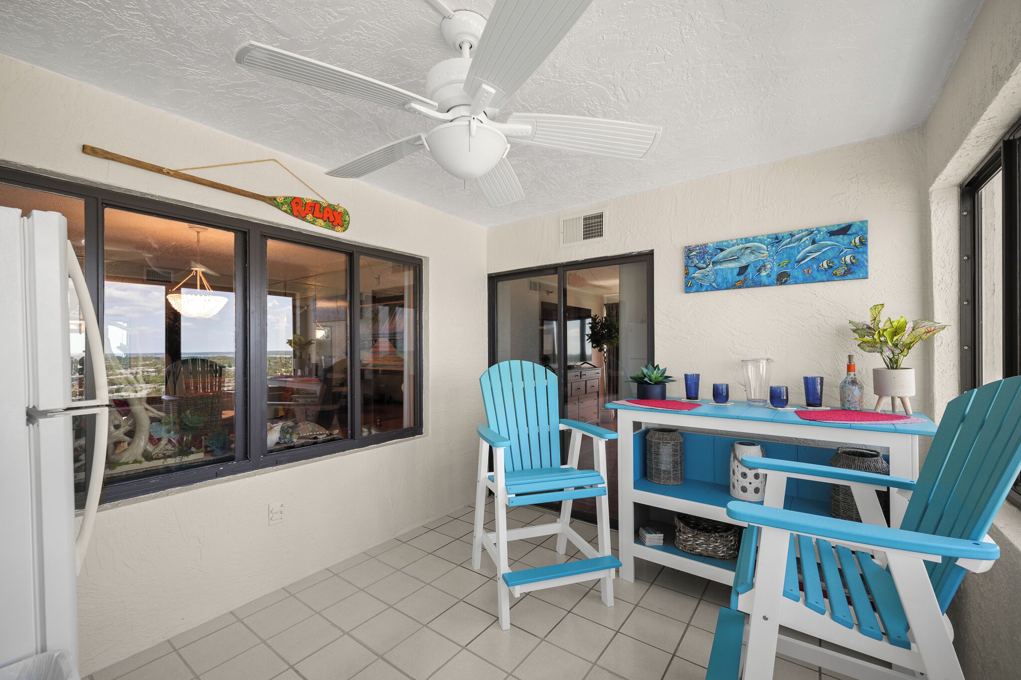 Un espace patio doté d’un ventilateur de plafond, d’une table avec des chaises et offrant une vue sur l’intérieur grâce à de grandes fenêtres.