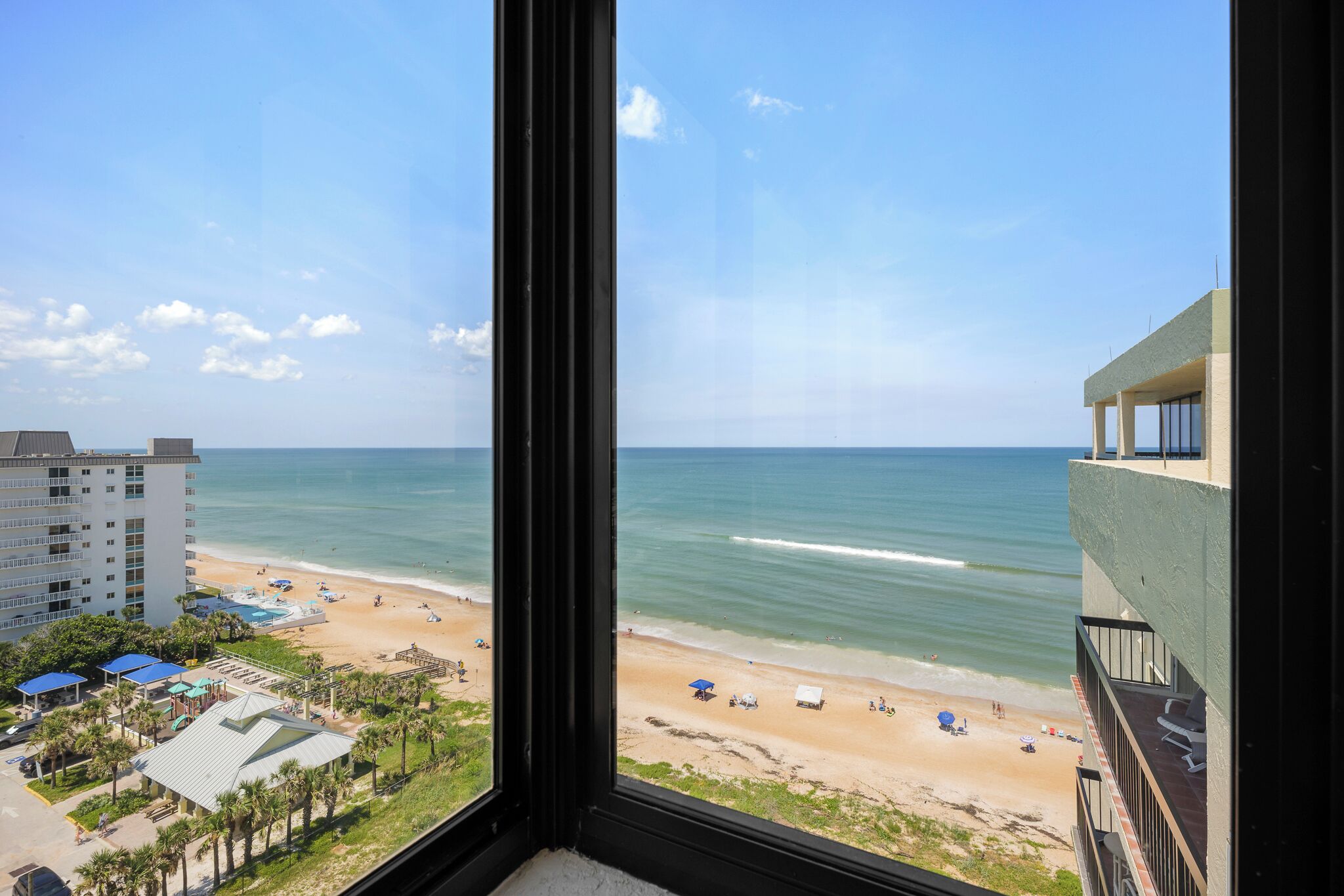 A beach view from a window overlooking a sandy beach with a few umbrellas and people.