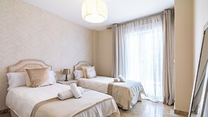 Une chambre d’hôtel avec deux lits, un lustre et une grande fenêtre avec des rideaux.