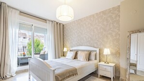 Une chambre à coucher avec un grand lit, des tables de chevet, une commode, une armoire et une vue sur l’extérieur.