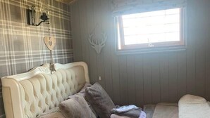 A cozy room with a tufted headboard bed, a window with blinds, plaid wallpaper, and a decorative antler wall piece. - Cute and Cosy Shepard hut With Wood Fuel hot tub (Kington)