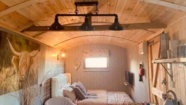 A cozy cabin interior with a bed, a window, and a rustic wooden ceiling. - Cute and Cosy Shepard hut With Wood Fuel hot tub (Kington)
