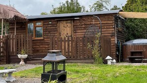 A rustic wooden cabin with a metal roof, a wooden fence, and a hanging chair. - Cute and Cosy Shepard hut With Wood Fuel hot tub (Kington)