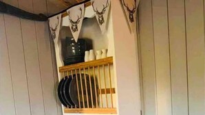A wooden dining table with two chairs, a shelf above holding plates and a bottle, and a small plant on the table. - Cute and Cosy Shepard hut With Wood Fuel hot tub (Kington)