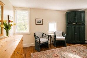A room with two wicker chairs, a wooden dresser, a green cabinet, and a patterned rug.