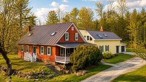 A two-story house with a front porch, a stone wall, and a driveway.