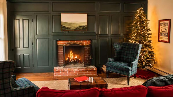A cozy living room with a fireplace, plaid furniture, a Christmas tree, and a framed picture on the wall.