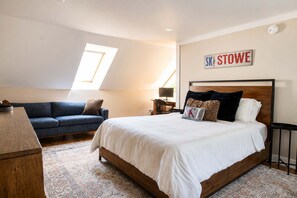 A bedroom with a bed, a sofa, a desk, and a skylight.
