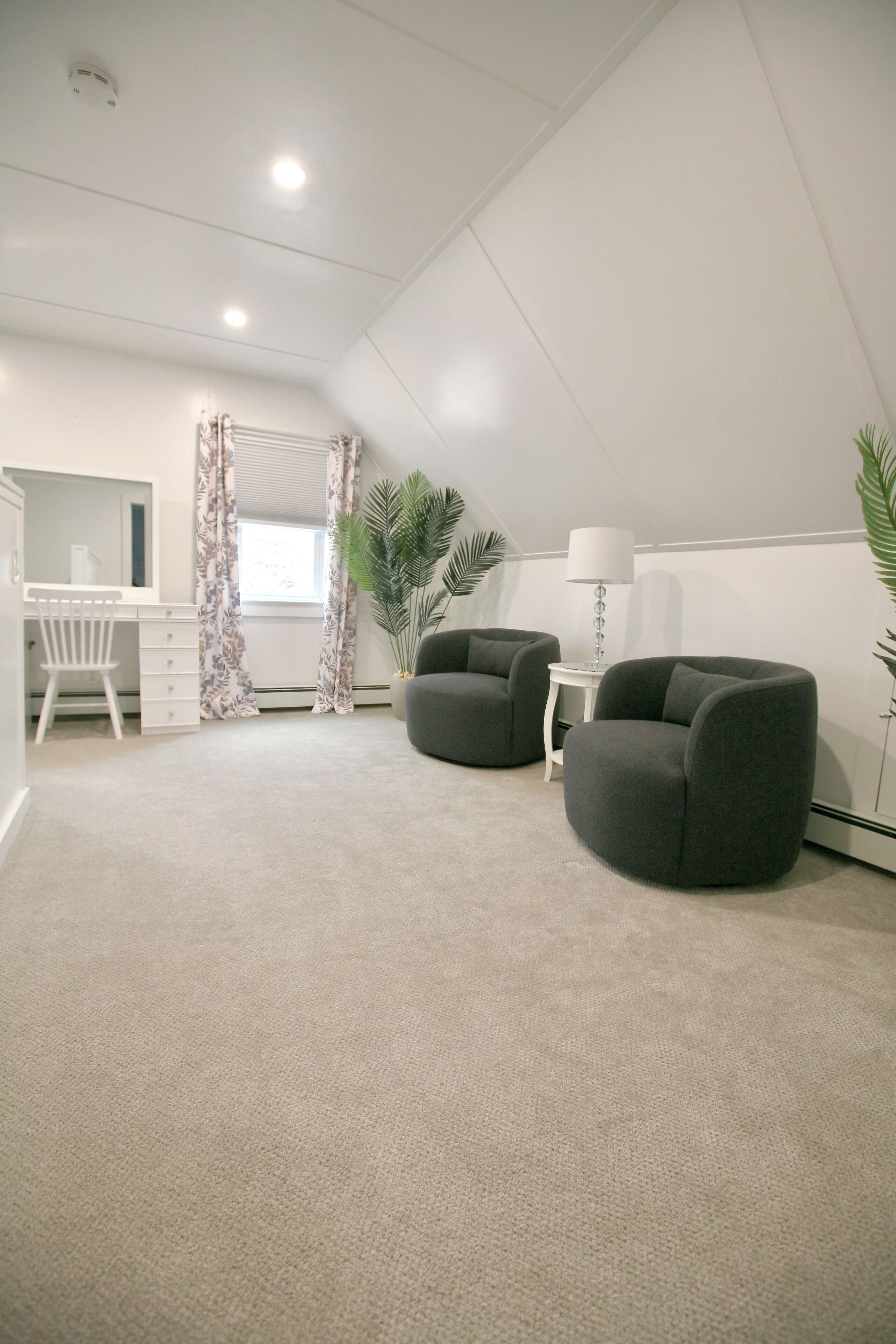 A modern room with a desk, two armchairs, a lamp, and a large window with curtains.