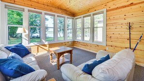 A room with a wooden ceiling, large windows, a white couch, and a table.