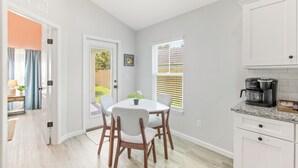 Una cocina moderna con gabinetes blancos, una cafetera y un comedor con mesa y sillas.