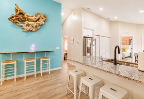A modern kitchen with a granite countertop, white bar stools, a neon sign, and a unique wall art piece.