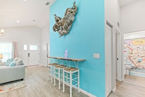 A modern living room with a light blue accent wall, a wooden coffee table with bar stools, and a neon sign.