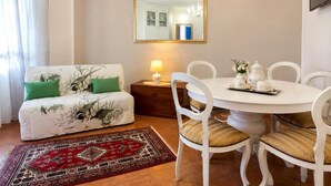 Un soggiorno con un divano, un tavolo da pranzo con sedie, un lampadario, uno specchio e un tappeto decorato.
