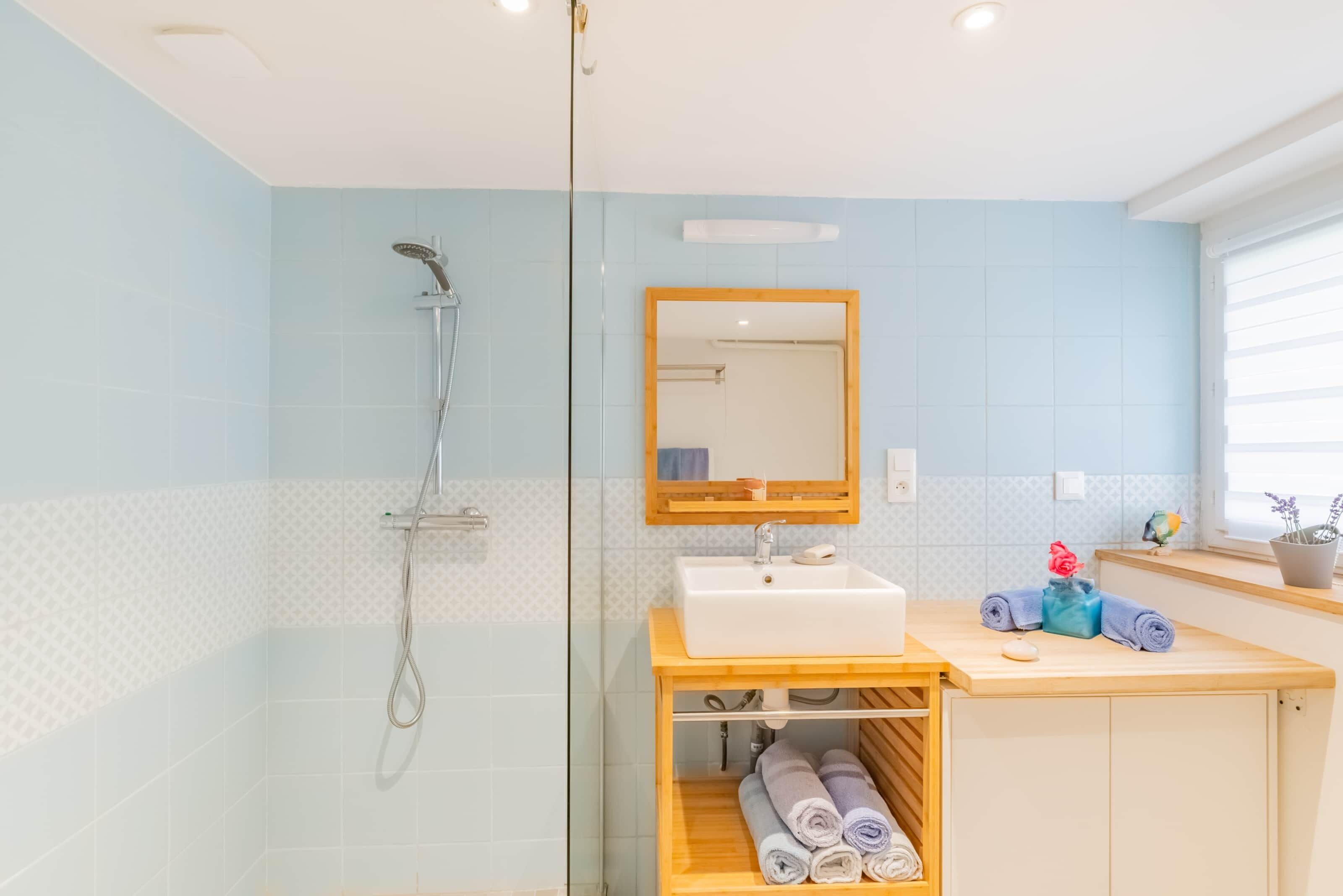 A bathroom with a glass shower enclosure, a white sink, a wooden vanity, and a mirror.