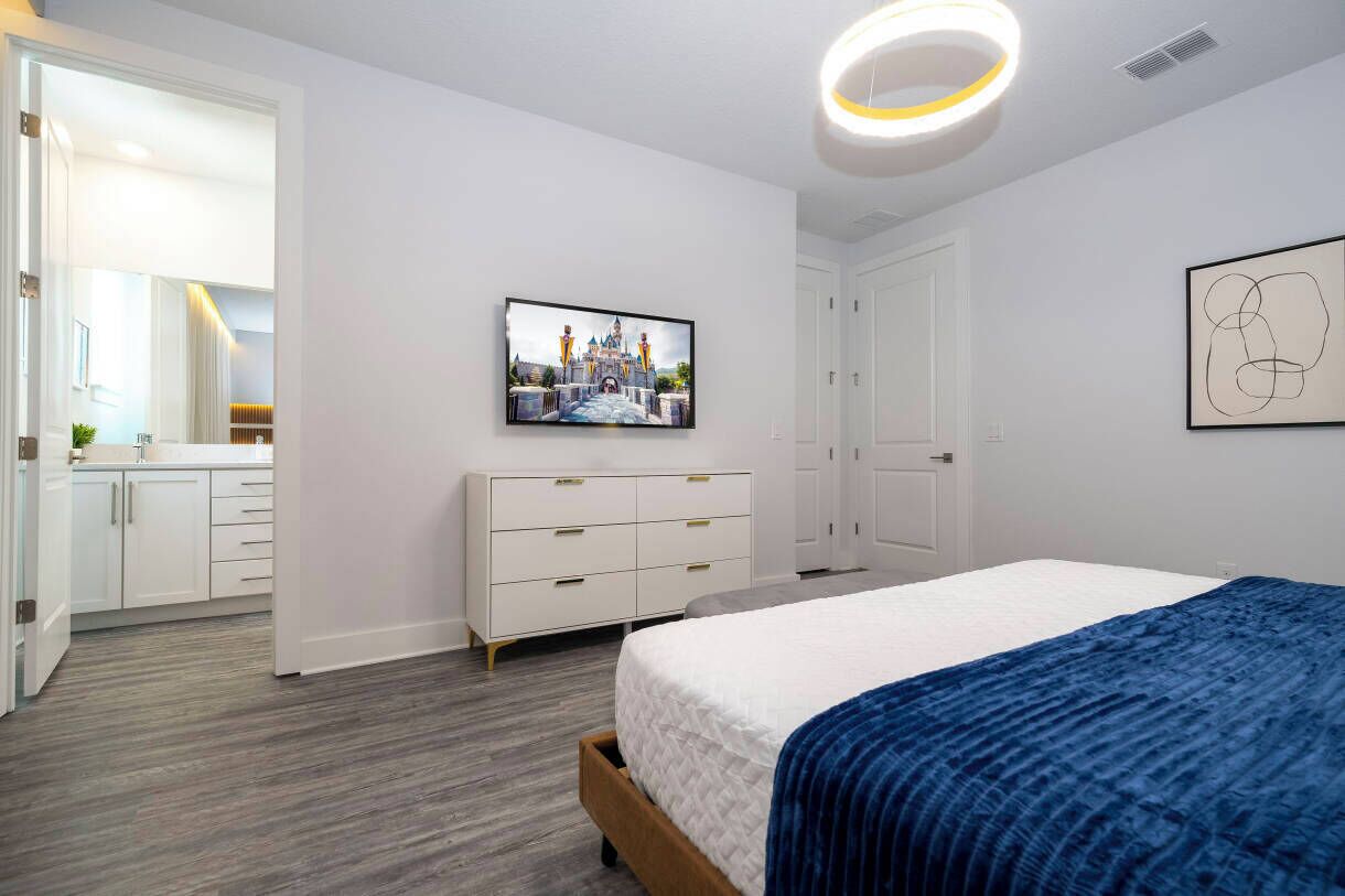 Une chambre à coucher moderne, équipée d’un lit, d’une commode, d’un téléviseur et d’une porte donnant accès à une salle de bain.