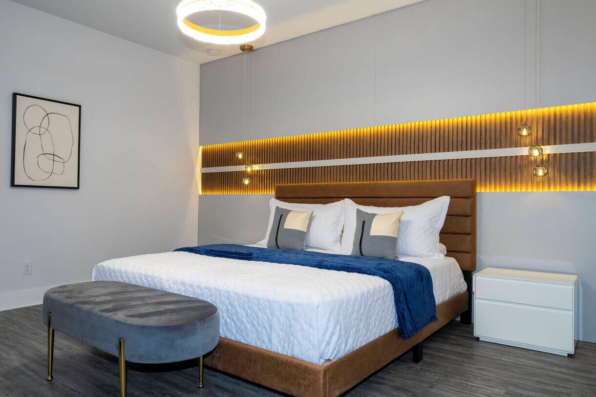 A modern bedroom with a large bed, a bedside table, and a wall-mounted light fixture.