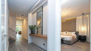Een moderne slaapkamer met een groot bed, nachtkastjes en een spiegel. Een gang leidt naar een trap.