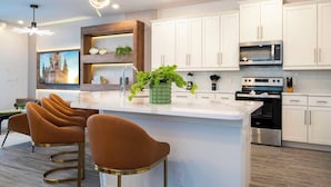 Een moderne keuken met witte kastjes, een centraal eiland met barstoelen, een magnetron, een oven en een decoratieve plant.