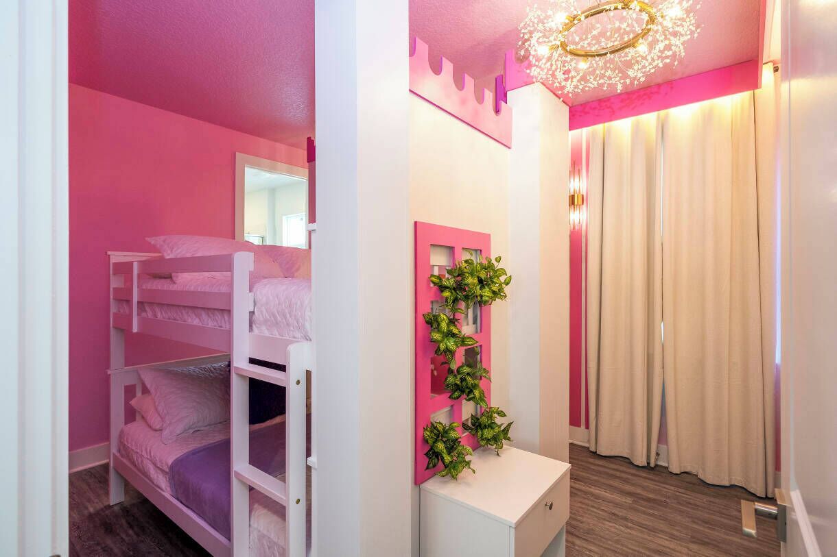Une chambre avec des lits superposés, un bureau blanc, un miroir et une plante fixée au mur.
