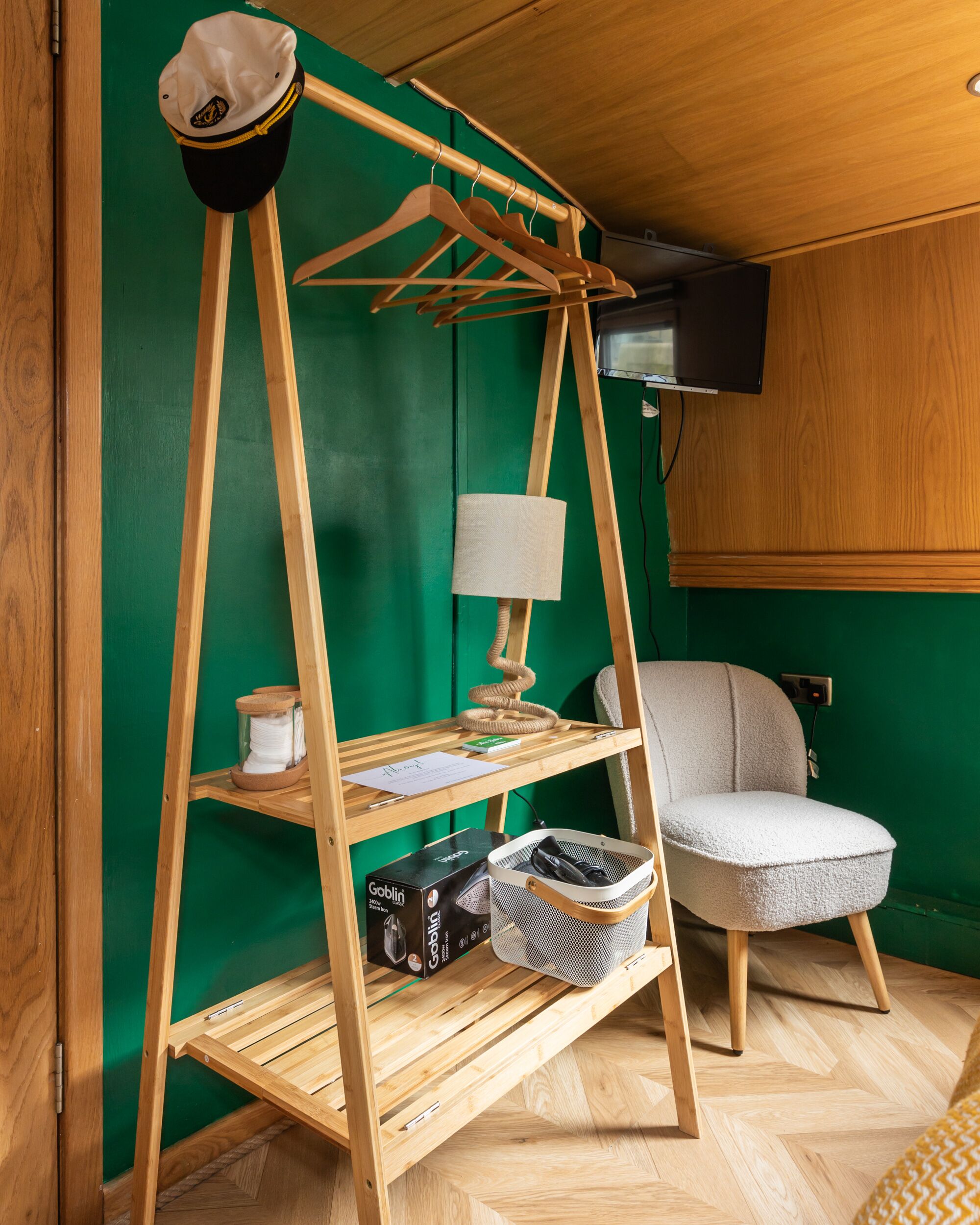 Ein Zimmer mit einem hölzernen Kleiderständer, einem Stuhl, einer Lampe und Regalen mit verschiedenen Gegenständen, darunter eine Kiste mit dem Aufdruck 'Goblin'.