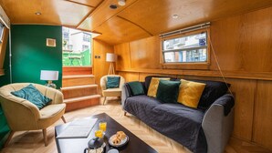 A cozy interior with a sofa, armchair, and a dining table with breakfast items. - 4* Luxury floating wide beam houseboat moored in Edinburgh city center. (Edinburgh)