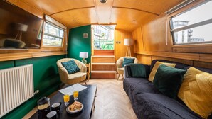 A cozy interior with a sofa, chairs, a dining table with breakfast, and a view through a window. - 4* Luxury floating wide beam houseboat moored in Edinburgh city center. (Edinburgh)