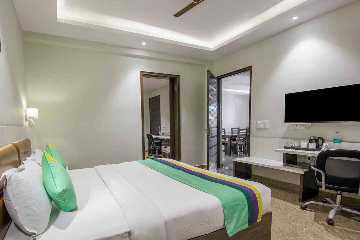 A hotel room with a bed, a desk, a chair, a TV, and a bathroom visible through an open door.