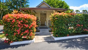 Un bâtiment à deux étages doté d’une entrée couverte, entouré d’une végétation luxuriante et de buissons en fleurs.