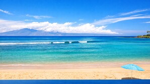 Une plage avec une eau d’un bleu limpide, un rivage sablonneux et une montagne en arrière-plan.