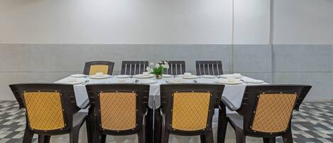 Une salle de conférence avec une table rectangulaire, des chaises noires à assise tissée et une nappe blanche.