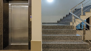 A modern elevator and a staircase with granite steps and metal railings. - Treebo Oscar (Rajkot)