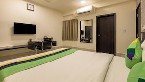 A hotel room with a bed, a desk, a chair, a television, a mirror, and an air conditioning unit. - Treebo Oscar (Rajkot)