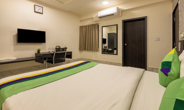 Une chambre d’hôtel équipée d’un lit, d’un bureau, d’une chaise, d’une télévision, d’un miroir et d’un appareil de climatisation.