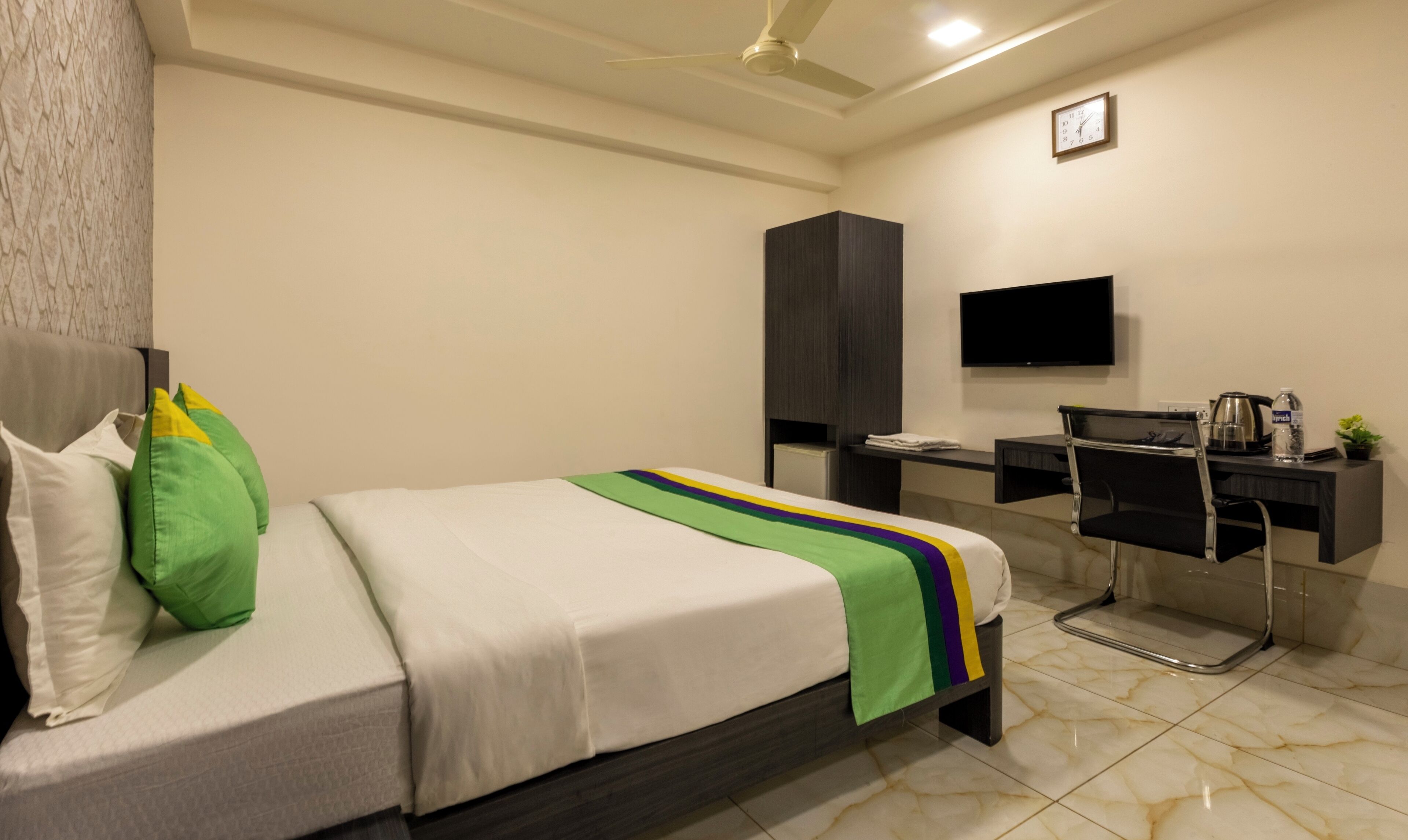 Una habitación de hotel con cama, escritorio, silla, televisor y ventilador de techo.
