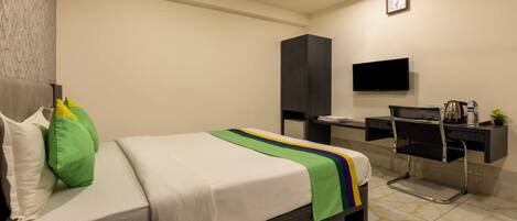 Una habitación de hotel con cama, escritorio, silla, televisor y ventilador de techo.