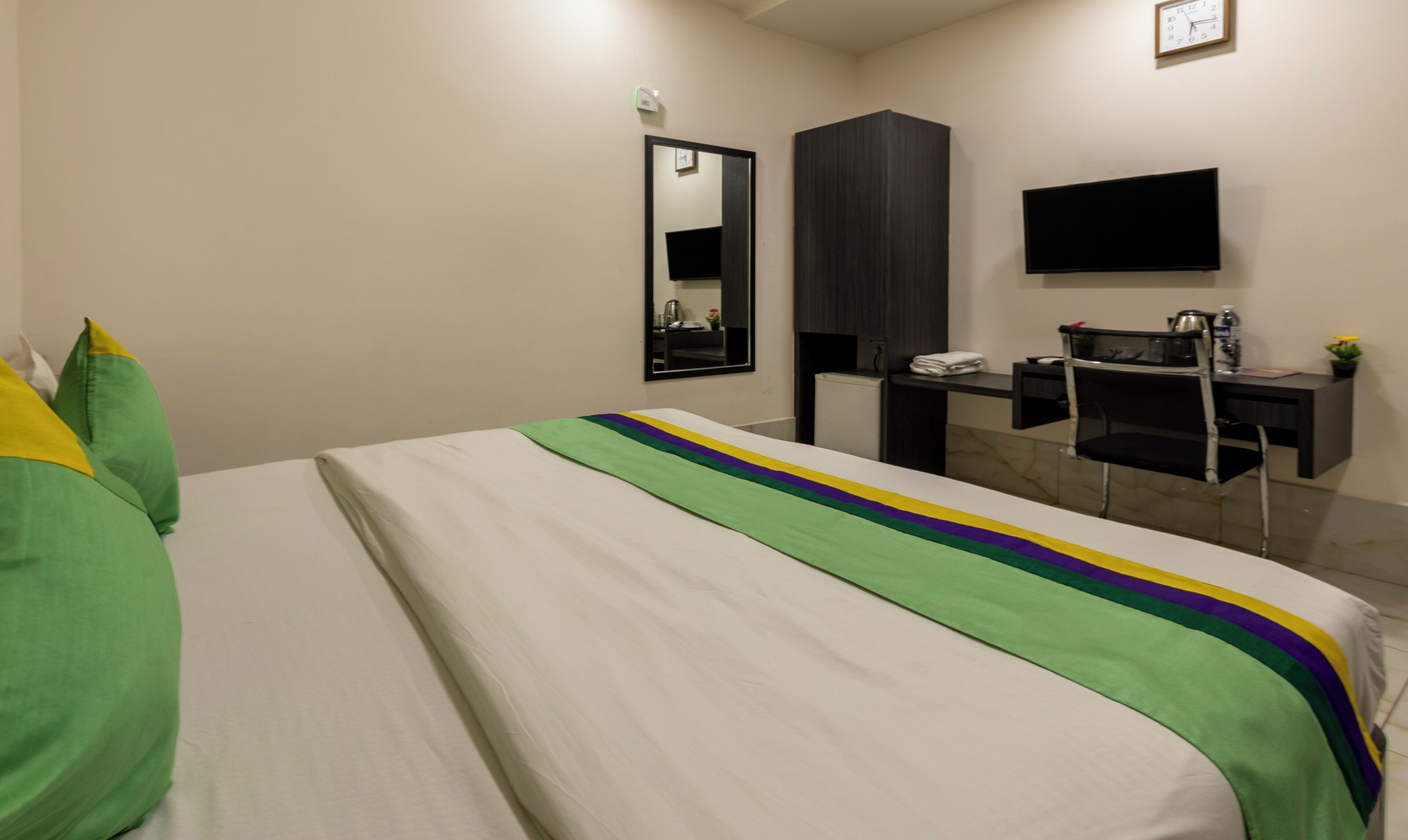 A hotel room with a bed, a desk, a chair, a flat-screen TV, and a mirror on the wall.