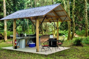 Un pavillon rustique en bois, doté d’un toit en métal, d’un évier intégré et d’un espace barbecue.